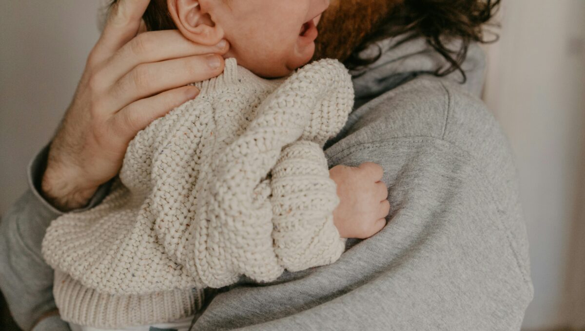 Ein Mann, der ein Baby das schreit auf dem Arm hält.